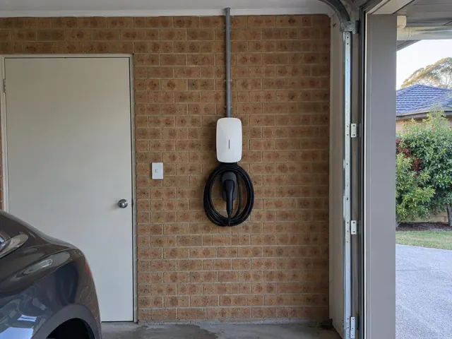 Wall-mounted EV charger on a brick garage wall beside a door in Niagara Park