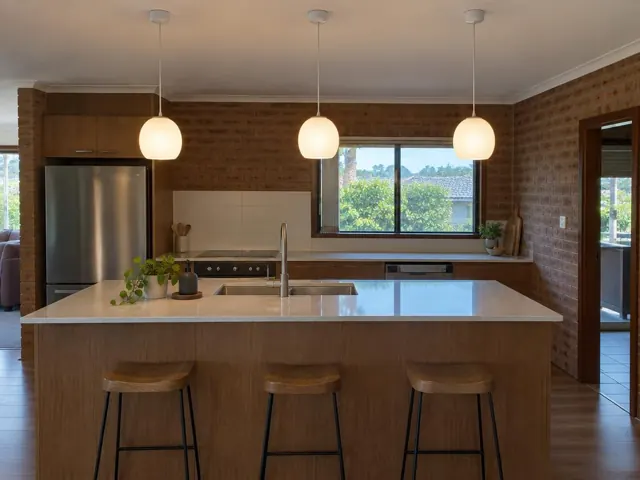 Kitchen island with three pendant lights, white benchtop and brick walls in Narara